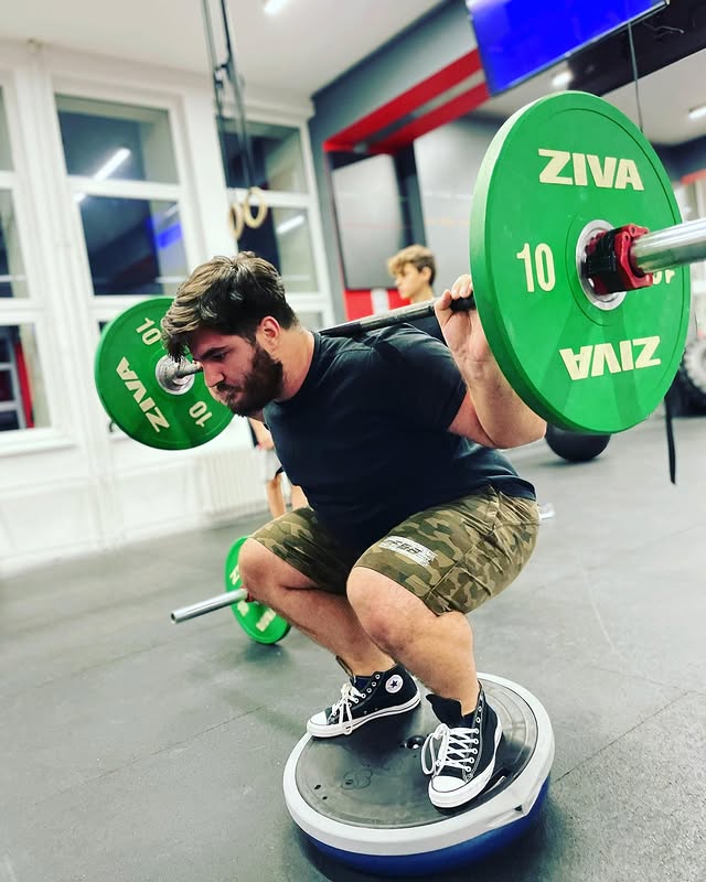 Klient Tomáše cvičí dřep s činkou na balanční podložce pro zlepšení síly a stability.